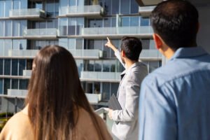 Gestionnaire montrant une façade d’immeuble moderne à des clients lors d’une visite avec un serrurier pour copropriété.